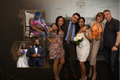 A group of five people posing together in front of a dark wall with two inset photos showing a couple and a bride and groom, likely a wedding photographer or family portrait service.