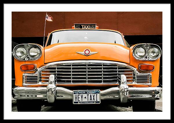 A framed art print featuring a front-facing photograph of a bright orange vintage Cadillac taxi with chrome details, a New York license plate reading 'HEY-TAXI', and a brown background.
