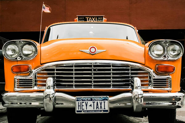 A vibrant orange classic 1950s Cadillac taxi with a chrome front grille and bumper, featuring a New York license plate that reads 'HEY-TAXI' and a taxi sign on the windshield.